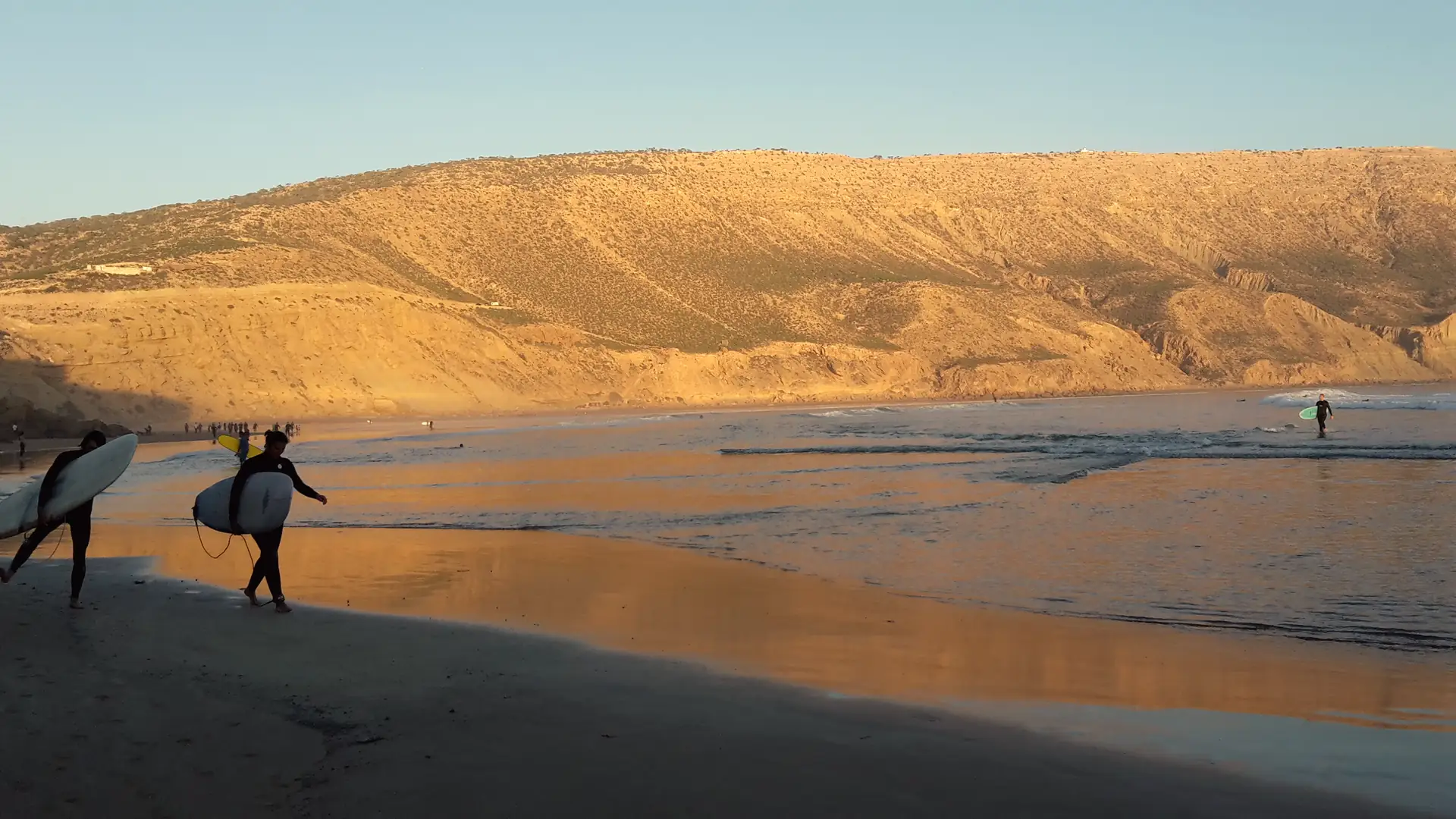 Two surfers walking along Imsouane beach at golden hour, boards under their arms